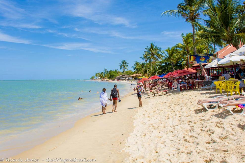 Imagem de casal caminhando mãos dadas na beira da Praia do Mutá.